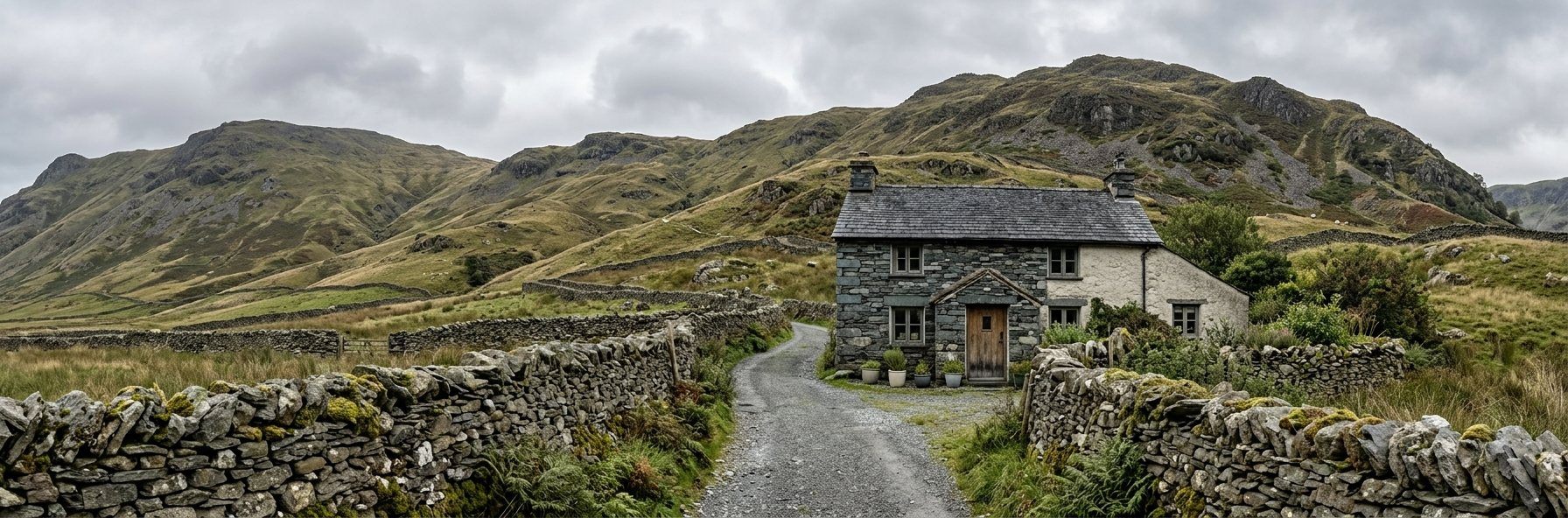 Fellgarth Cottage at the end of a gravel track, a slate and whitewashed stone cottage with dry-stone walls either side and open fells rising behind.